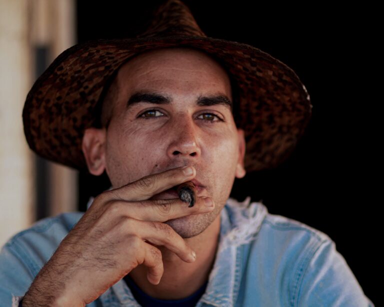 Close-up portrait of a man wearing a straw hat and smoking a cigar, showcasing a thoughtful expression.